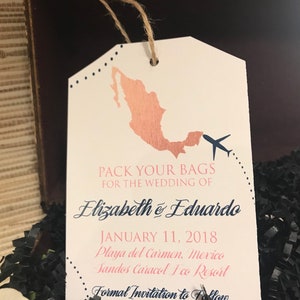 May include: A luggage tag with a rose gold outline of Mexico and a blue airplane. The tag says "Pack your bags for the wedding of Elizabeth & Eduardo, January 11, 2018, Playa del Carmen, Mexico, Sandos Caracol Eco Resort, Formal Invitation to Follow."