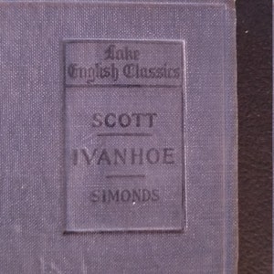 May include: A close-up of a book cover with the title "Ivanhoe" by Scott. The book is part of the "Lake English Classics" series. The cover is a muted blue-gray color with embossed text.