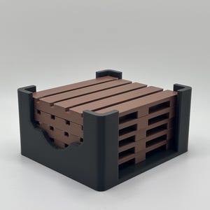 May include: A set of brown miniature pallet coasters in a black holder. The coasters are made of horizontal wooden slats, stacked neatly in a square black holder. The holder has a curved cutout on one side for easy access to the coasters.