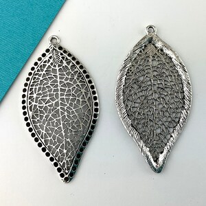 May include: Two silver filigree leaf-shaped pendants with a delicate, intricate design. The pendants have a hole at the top for hanging.