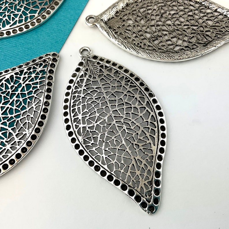May include: Three silver filigree leaf-shaped pendants with a textured surface and a hole at the top for hanging.