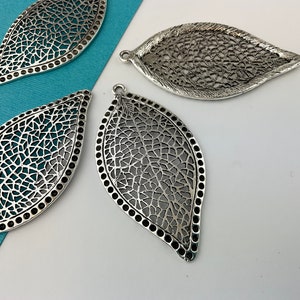 May include: Four silver filigree leaf-shaped metal charms with a textured design. The charms have a hole at the top for hanging.