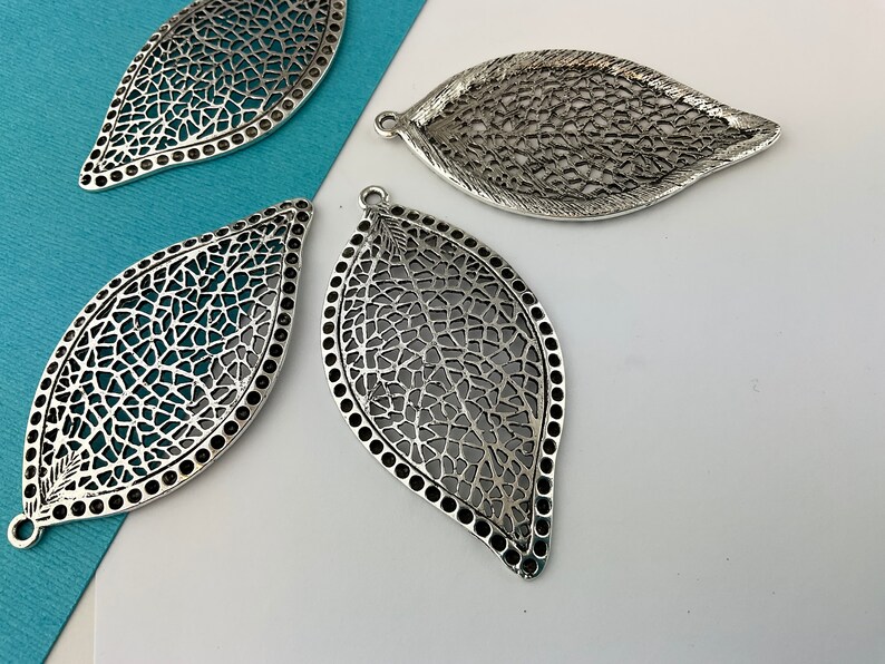 May include: Four silver filigree leaf-shaped metal charms with a textured design. The charms have a hole at the top for hanging.