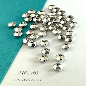 May include: A pile of silver-toned metal beads with a faceted design. The beads are scattered on a white surface. The text "PWT 761" and "@BlueEchoBeads" is visible in the image.
