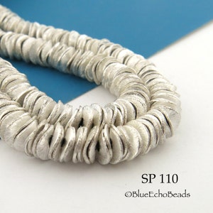 May include: A strand of silver-toned metal beads, each bead is a flat disc with a textured surface. The beads are arranged in a circular pattern, creating a layered effect. The image includes the text "SP 110 ©BlueEchoBeads".