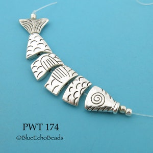 May include: Silver-toned fish-shaped beads strung on a clear elastic cord. The beads are detailed with scales and other patterns. The text "PWT 174" and "©BlueEchoBeads" is printed below the beads.