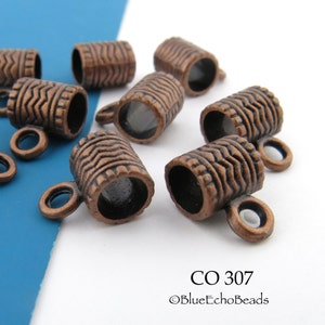 May include: Close-up of several copper-colored barrel-shaped beads with textured wave patterns. Each bead has a small loop attached. The beads are scattered on a white and blue surface. The text "CO 307" is visible.