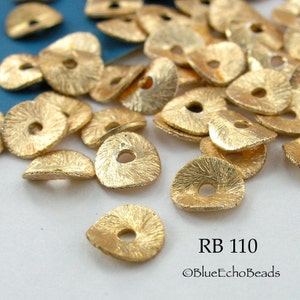 May include: A close-up of a pile of gold-colored metal beads with a textured surface. The beads are shaped like a teardrop with a hole in the center. The beads are labeled "RB 110" and "©BlueEchoBeads".