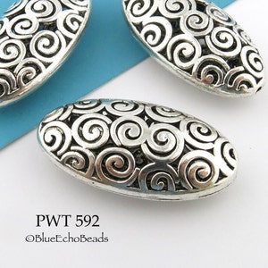 May include: Three silver oval-shaped beads with a swirl design. The beads are about 1 inch long and have a delicate, intricate pattern. PWT 592 ©BlueEchoBeads