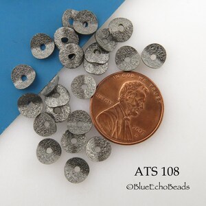 May include: Close-up of a collection of small, textured, gray metal disc beads with a central hole. A U.S. penny is included for size comparison. The text "ATS 108" and "©BlueEchoBeads" are visible.