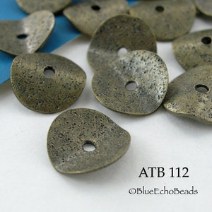 May include: A group of antique brass-colored metal beads with a textured surface and a hole in the center. The beads are shaped like a flat, slightly curved disc. The beads are arranged on a white surface. ATB 112 ©BlueEchoBeads