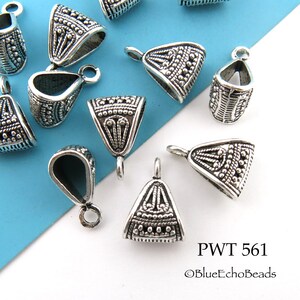 May include: Silver-toned metal pendant caps with an intricate design. The caps are triangular in shape with a loop at the top for attaching a pendant. The caps are arranged on a blue and white surface.  PWT 561 ©BlueEchoBeads
