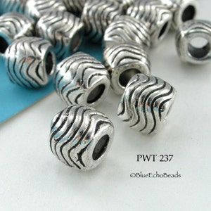 May include: A close-up of a pile of silver metal beads with a wavy pattern. The beads have a hole in the center and are approximately 1 cm in diameter. The text "PWT 237 ©BlueEchoBeads" is visible in the lower right corner of the image.