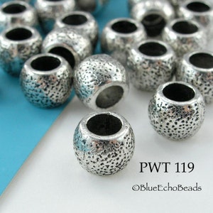 May include: A close-up of a group of silver metal beads with a textured surface. The beads have a hole in the center and are approximately 10mm in diameter. The beads are arranged on a blue and white surface. The text "PWT 119" and "©BlueEchoBeads" is visible in the image.