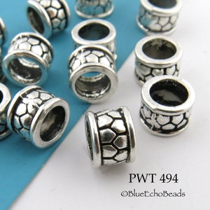May include: A close-up of silver metal beads with a textured hexagonal pattern. The beads are about 1/2 inch in diameter and have a hole in the center. The beads are arranged in a random pattern on a blue and white surface. PWT 494 ©BlueEchoBeads