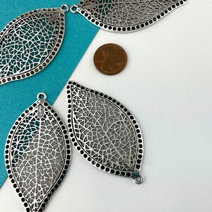 May include: Four silver filigree leaf-shaped metal charms with a textured design. The charms have a hole at the top for hanging.