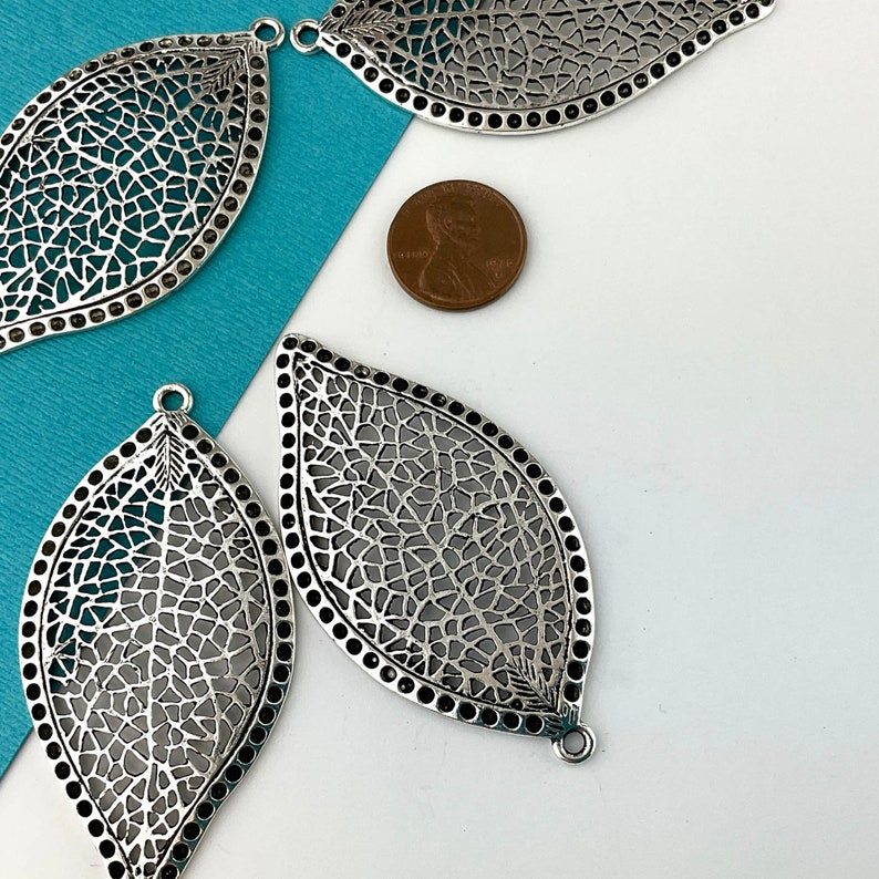 May include: Four silver filigree leaf-shaped metal charms with a textured design. The charms have a hole at the top for hanging.
