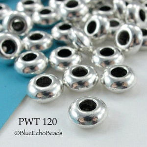 May include: A close-up of a pile of silver-toned metal beads with a round shape and a hole in the center. The beads are arranged in a random pattern on a blue surface. The text "PWT 120" and "©BlueEchoBeads" is visible in the lower left corner of the image.