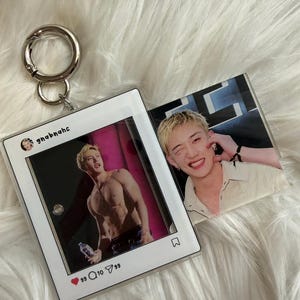 Könnte beinhalten: Ein quadratischer Acryl-Schlüsselanhänger mit zwei doppelseitigen Fotoeinsätzen einer Person mit blonden Haaren. Eine Seite imitiert einen Social-Media-Beitrag mit dem Benutzernamen gnabnahc, einem Foto einer oberkörperfreien Person und Interaktionssymbolen.
