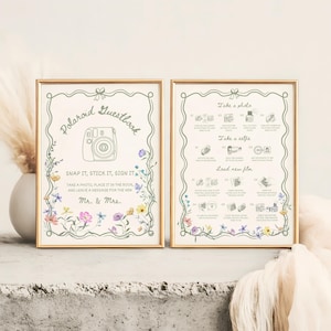 May include: Two framed signs with gold borders. The left sign reads "Polaroid Guestbook" with instructions and floral accents. The right sign has photo-taking instructions. Both signs are on a concrete surface.