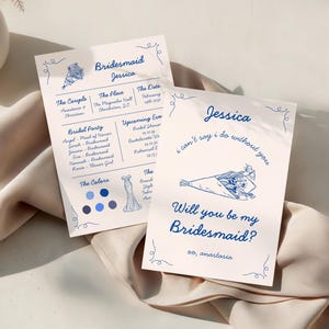 May include: Two light pink cards with blue text and illustrations. One card reads "Bridesmaid Jessica" with event details. The other says "Will you be my Bridesmaid?" with a bouquet illustration. The cards are on a light pink fabric.