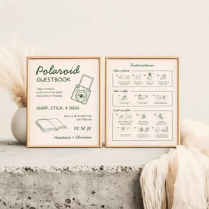 May include: Two framed signs with gold borders. The left sign reads "Polaroid Guestbook" with instructions and a camera illustration. The right sign has photo instructions. The signs are on a white surface.