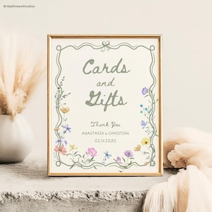 May include: A framed sign with the words "Cards and Gifts" in a soft green font. The sign is decorated with a floral border and includes the text "Thank You" and names and a date. The frame is gold.