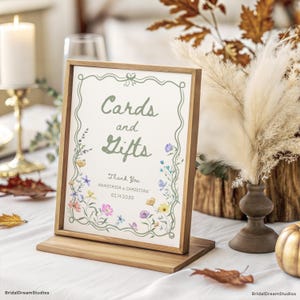 May include: A wooden framed sign with the words "Cards and Gifts" in a script font. The sign is decorated with floral illustrations and includes the text "Thank You Anastasia & Christian 02.14.2030". The sign is displayed on a wooden stand.
