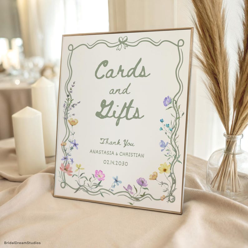 May include: A rectangular sign with the words "Cards and Gifts" in green script, framed by a floral border. The sign includes the text "Thank You" and names, with a date. The background is off-white, and the frame is a light brown.