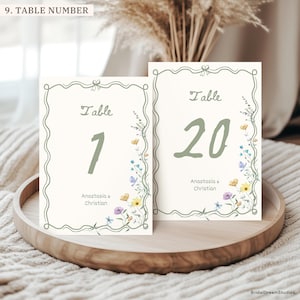 May include: Two rectangular table number cards with off-white backgrounds, featuring a sage green wavy border, the word Table, the numbers 1 and 20 in sage green, and the names Anastasia & Christian with small watercolor wildflowers on the side.