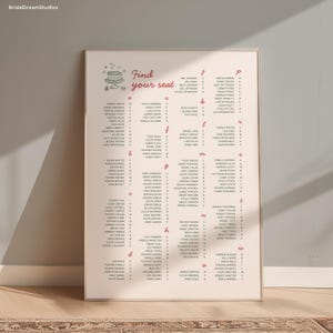 May include: A framed seating chart with a light pink background. The words "Find your seat" are in red script above a list of names. The names are organized alphabetically and are in black font.