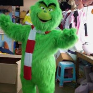 Könnte beinhalten: Ein grünes, flauschiges Grinch-Maskottchen-Kostüm mit einem rot-weiß gestreiften Schal. Das Kostüm steht auf einem hellen Boden.