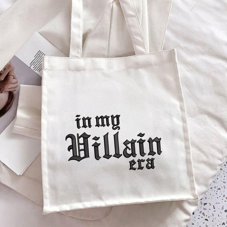 May include: White canvas tote bag with black text that reads "in my Villain era".