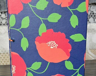 May include: A floral journal with a navy blue background and a pattern of red poppies and green leaves. The journal is bound with orange thread and has a hard cover.