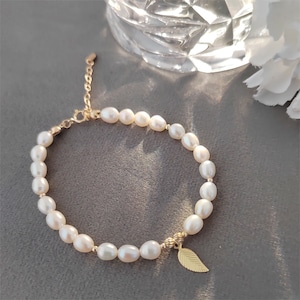 May include: A delicate gold bracelet with a small leaf charm and a strand of white pearls.