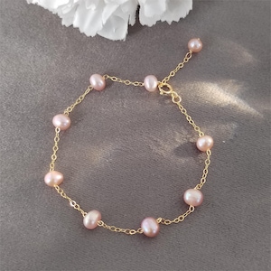 May include: A delicate gold chain bracelet with pink pearls. The bracelet has a lobster clasp closure.