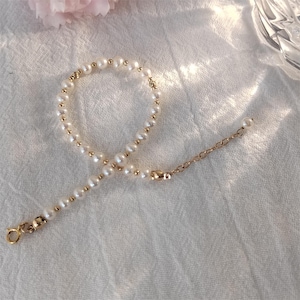 May include: A delicate gold chain bracelet with a strand of white pearls. The bracelet has a lobster clasp closure.