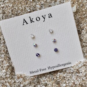 Peut inclure: Un ensemble de six boucles d'oreilles hypoallerg&eacute;niques avec des cristaux transparents et violets. Les boucles d'oreilles sont pr&eacute;sent&eacute;es sur une carte blanche avec le mot "Akoya" et le texte "Metal-Free Hypoallergenic".