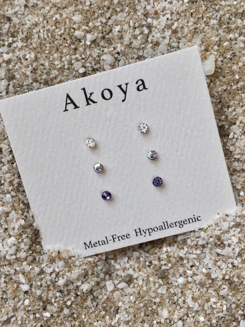 Peut inclure: Un ensemble de six boucles d'oreilles hypoallerg&eacute;niques avec des cristaux transparents et violets. Les boucles d'oreilles sont pr&eacute;sent&eacute;es sur une carte blanche avec le mot "Akoya" et le texte "Metal-Free Hypoallergenic".