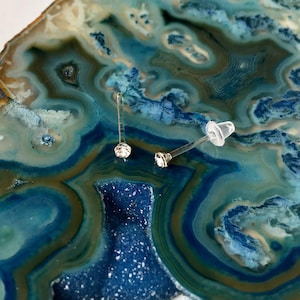 Peut inclure: Deux boucles d'oreilles en argent avec des pierres de cristal claires sur un fond d'agate bleu et vert.