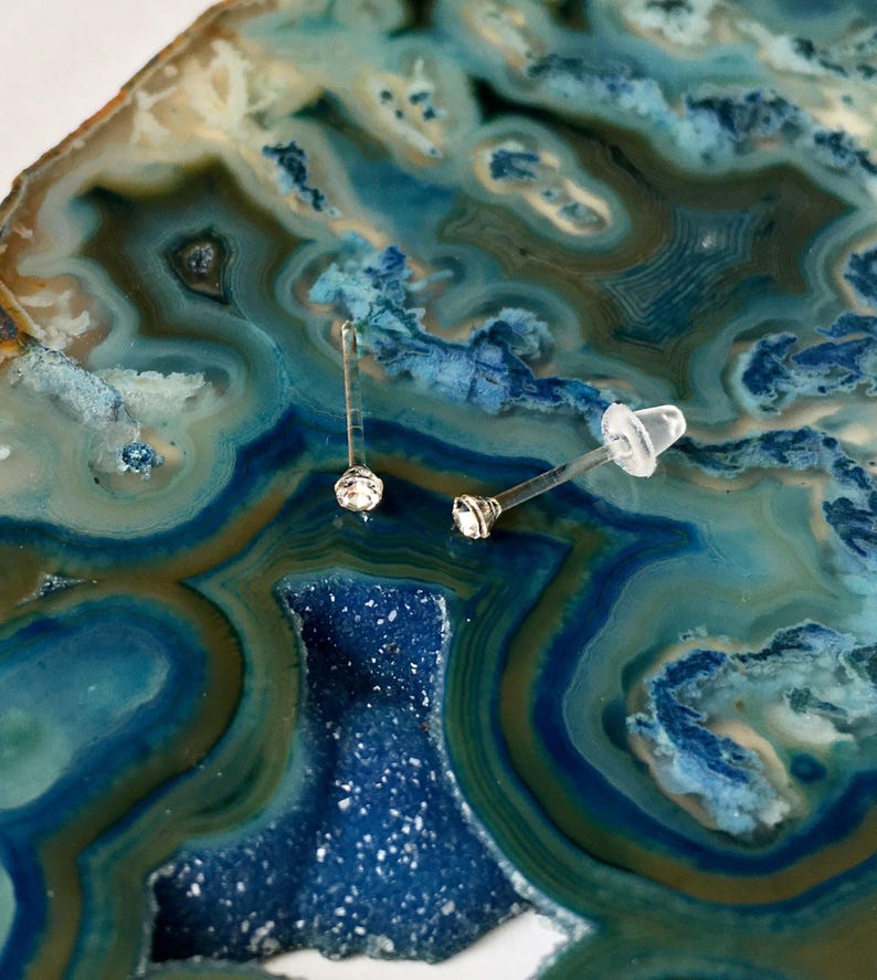 Peut inclure: Deux boucles d'oreilles en argent avec des pierres de cristal claires sur un fond d'agate bleu et vert.