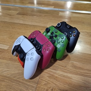 Peut inclure: Quatre manettes de jeu vidéo de couleurs différentes empilées les unes sur les autres. Les manettes sont blanches, rouges, vertes et noires.