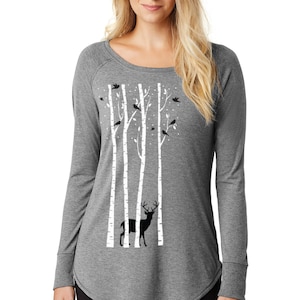 May include: A gray long-sleeved shirt with a white birch tree and deer silhouette design. The shirt has a scoop neck and a curved hem.