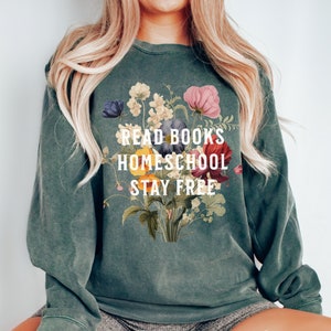 Op de afbeelding: Een groen sweatshirt met een bloemenontwerp en de tekst "Read Books Homeschool Stay Free".