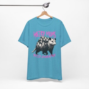 May include: A light blue t-shirt with a graphic of a possum carrying a group of baby possums on its back. The text "Weird Moms Build Character" is printed in pink below the graphic.