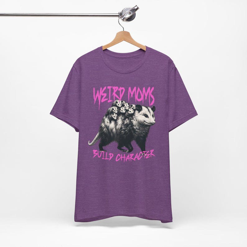 May include: Purple t-shirt with a graphic of a possum carrying baby possums on its back. The text "Weird Moms Build Character" is printed in pink below the image.