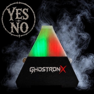 May include: A black pyramid-shaped device labeled GHOSTRONIX with a glowing green and red top section. Above the device, a circular emblem features the text YES NO in a distressed font. The entire object is surrounded by swirling white smoke.
