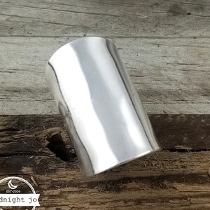 May include: A silver cuff bracelet with a smooth, polished finish. The bracelet is made of metal and has a cylindrical shape.