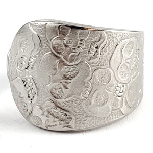 May include: A silver ring with a skull design. The ring is wide and has a curved shape. The skulls are embossed and detailed.