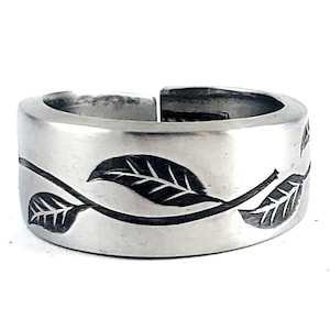 May include: A silver ring with a vine and leaf design engraved around the band.